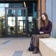 Person sitting outside on campus working on laptop