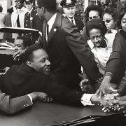 Martin Luther King Jr. in a car and shaking hands with people standing nearby